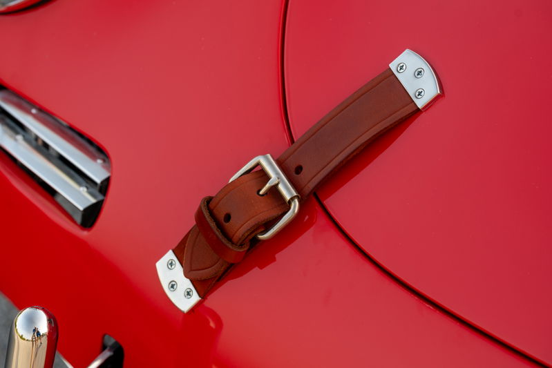 1965 Porsche 356C in Signal Red with a brown leather hood strap and chrome trim.