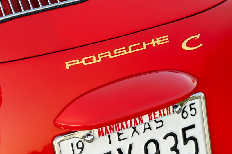 Golden "Porsche C" emblem on a Signal Red 1965 Porsche 356C with a Texas license plate.