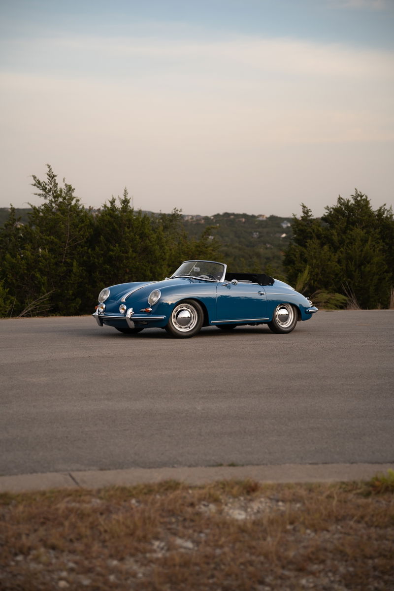 A royal blue 1960 Porsche 356B Roadster with chrome rims parked on asphalt.