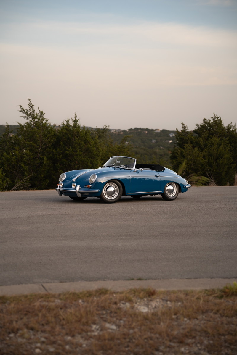 A royal blue 1960 Porsche 356B Roadster with chrome rims parked on asphalt.