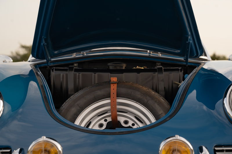 Blue 1960 Porsche 356B Roadster front trunk with spare tire and chrome rims.