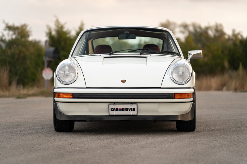 Front view of a white 1974 Porsche 911 coupe with black trim and a "Car and Driver" license plate.
