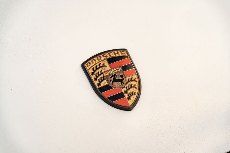 Close up of a vintage Porsche crest badge on a white 1974 Porsche 911 Coupe.