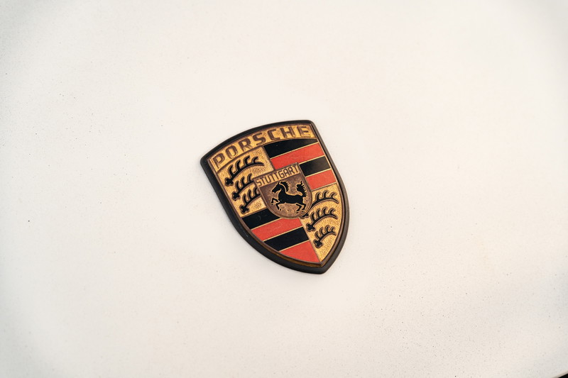 Close up of a vintage Porsche crest badge on a white 1974 Porsche 911 Coupe.