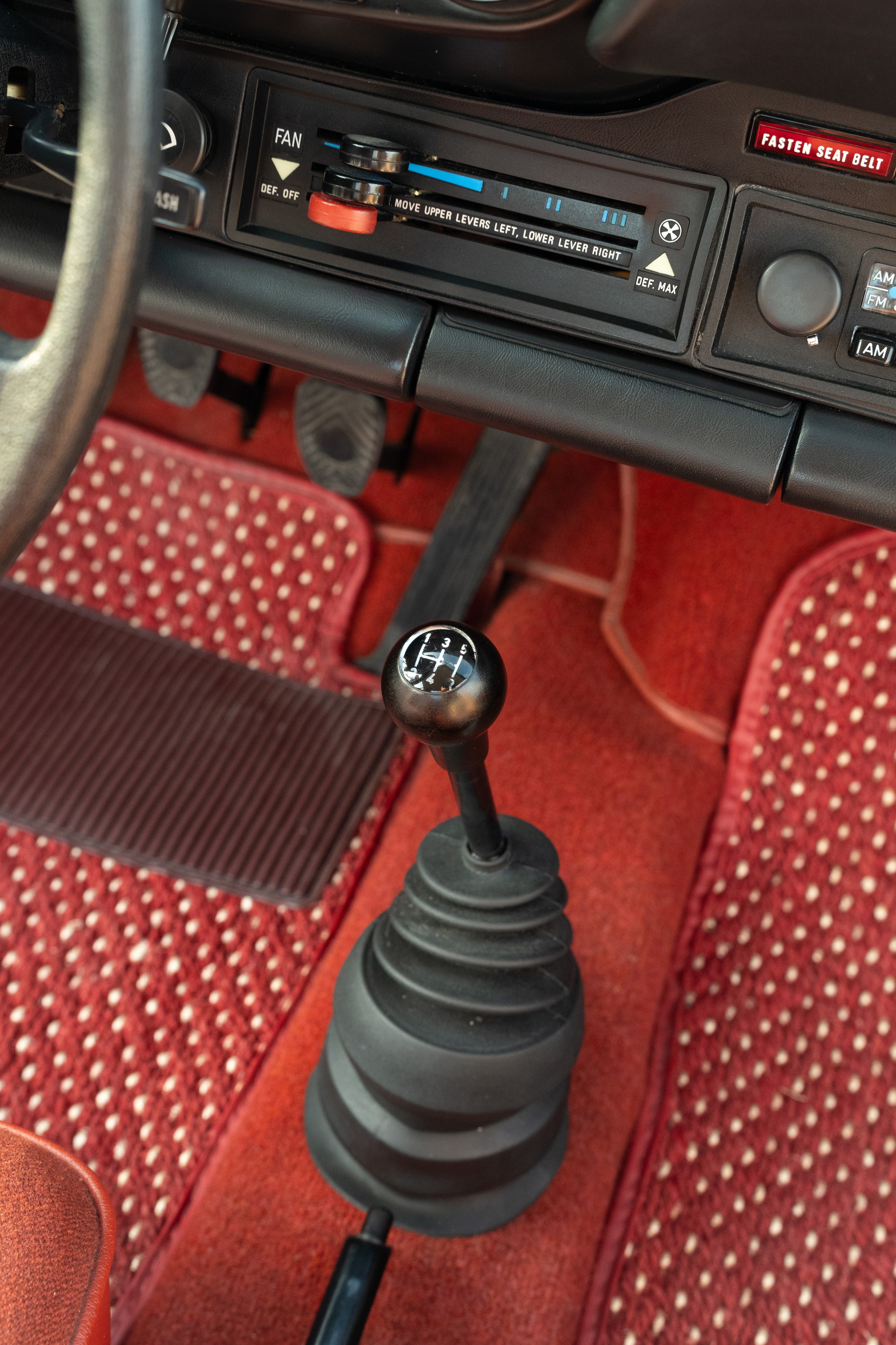 Interior shot of a 1974 Porsche 911 Coupe with red carpet and manual shifter.