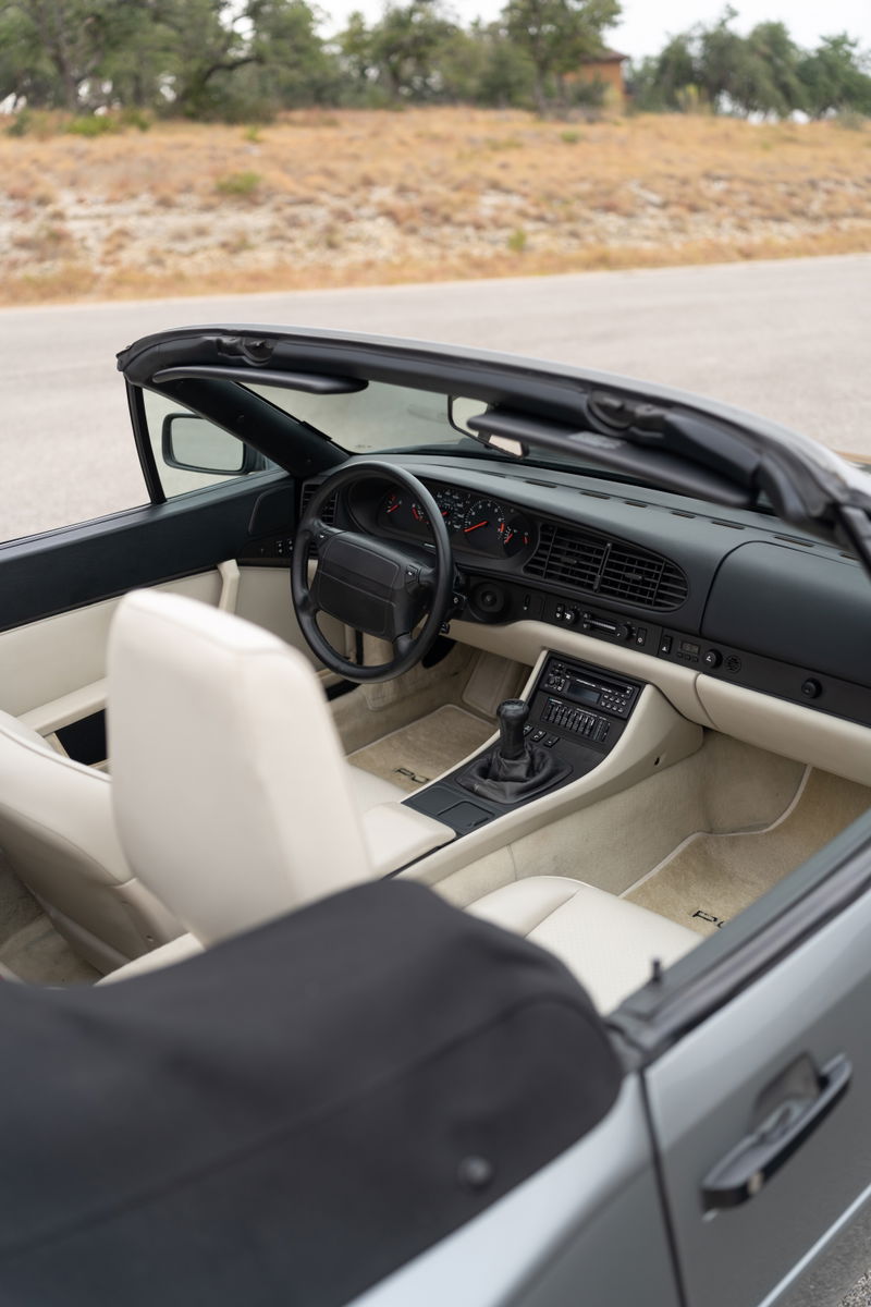 Interior view of a 1990 Porsche 944 S2 Cabriolet in Titanium Metallic with light beige leather seats and black soft-top.