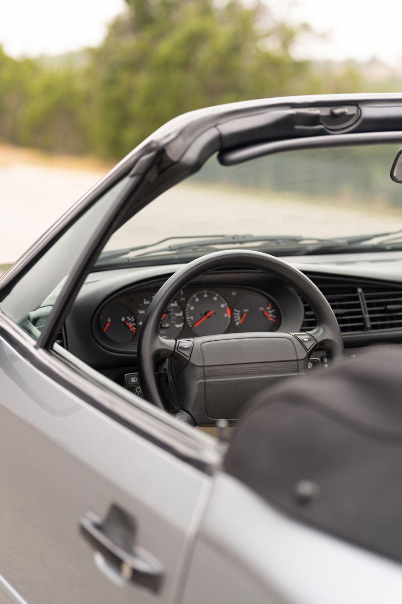 Close-up interior of a silver 1990 Porsche 944 S2 Cabriolet, showing the steering wheel and dashboard.