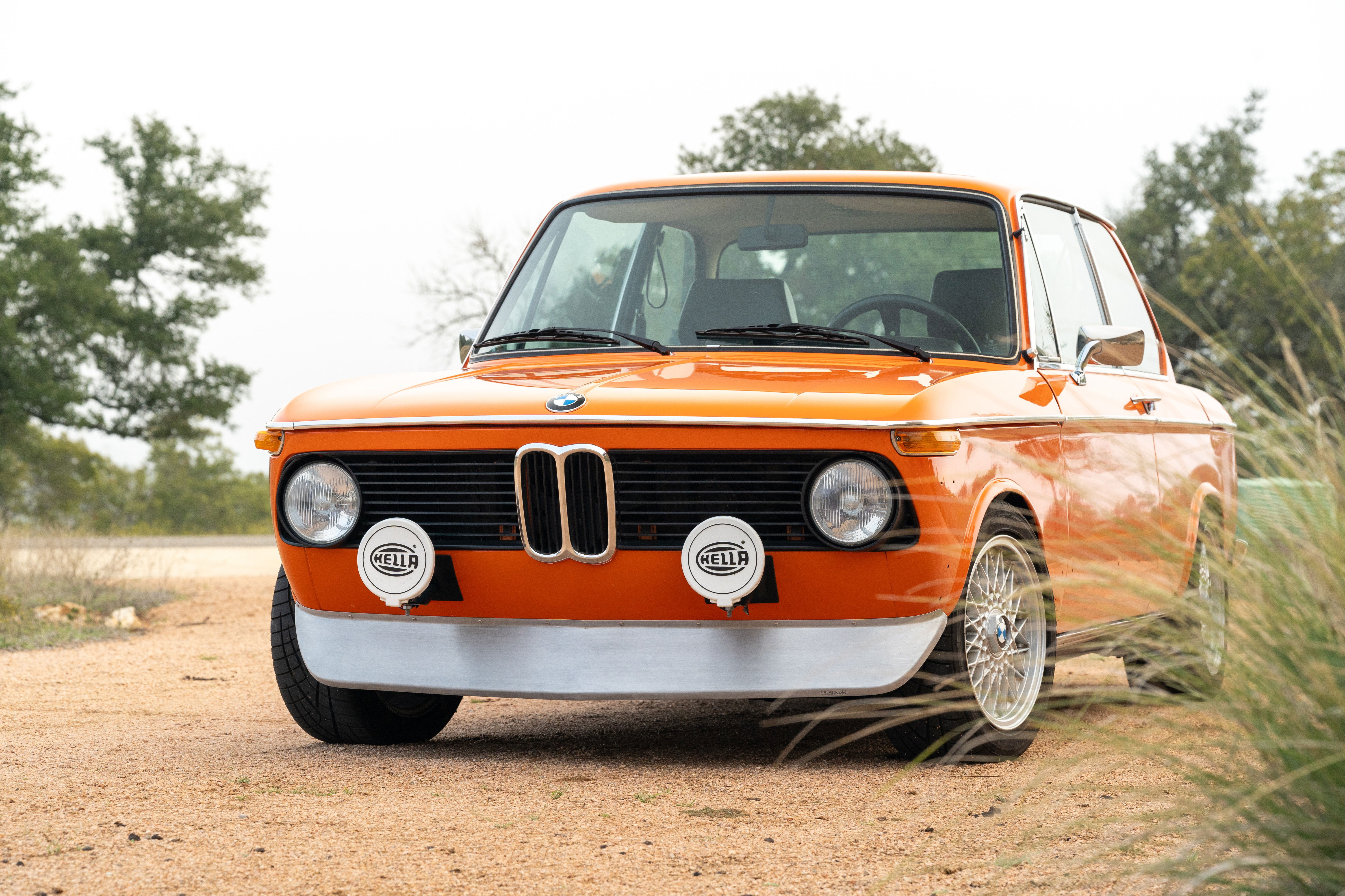 1976 Inka Orange BMW 2002 with chrome trim, Hella fog lights, and mesh rims.