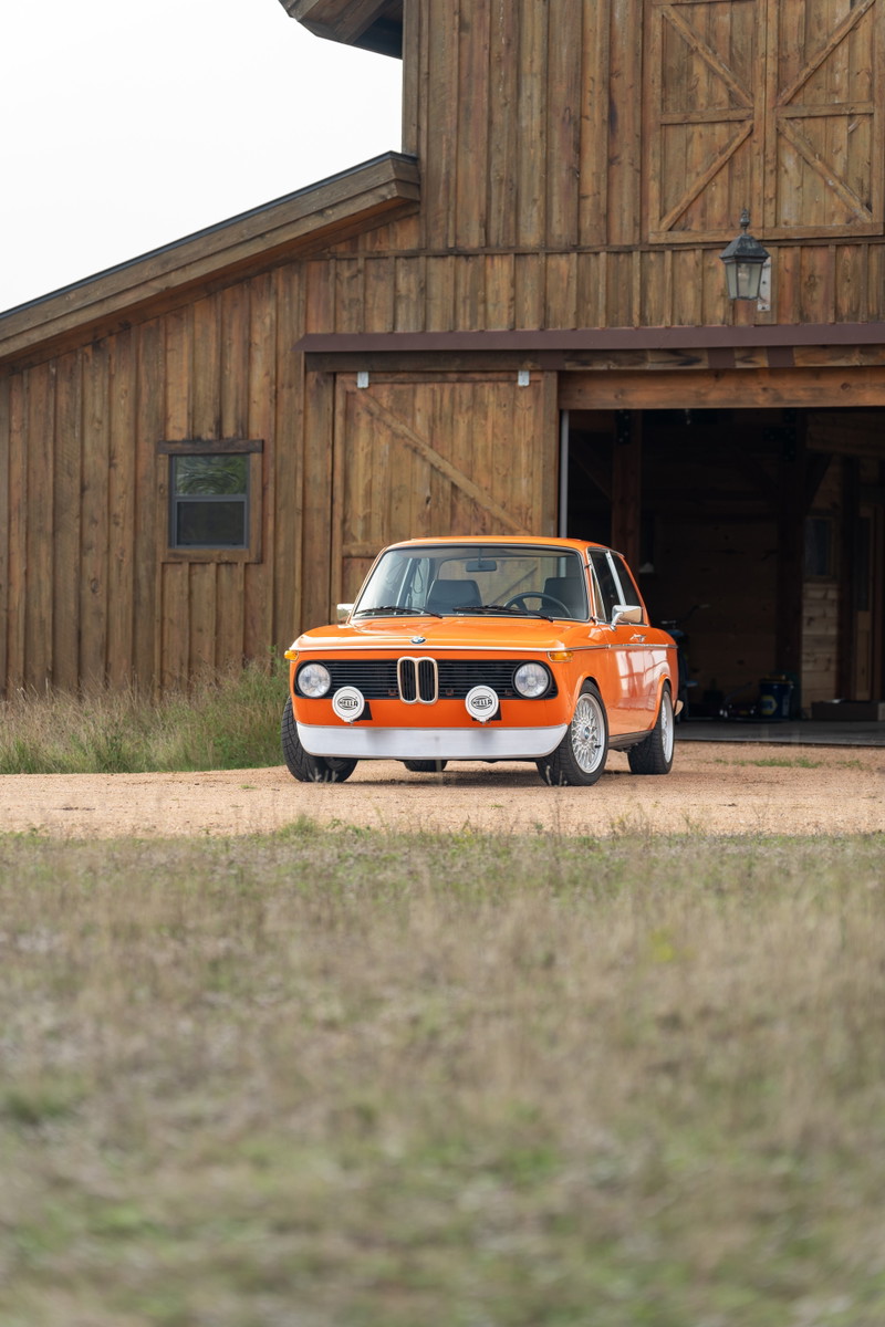 Orange 1976 BMW 2002 with vintage rally lights, chrome trim, and classic rims.