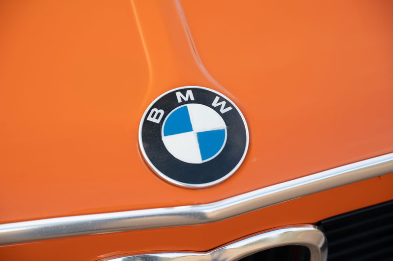 Close up of the BMW emblem on the hood of an Inka Orange 1976 BMW 2002.