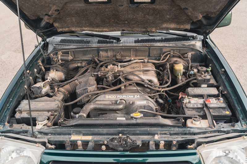 Open hood of a green 2000 Toyota 4Runner showing the 3.4L V6 engine and battery.