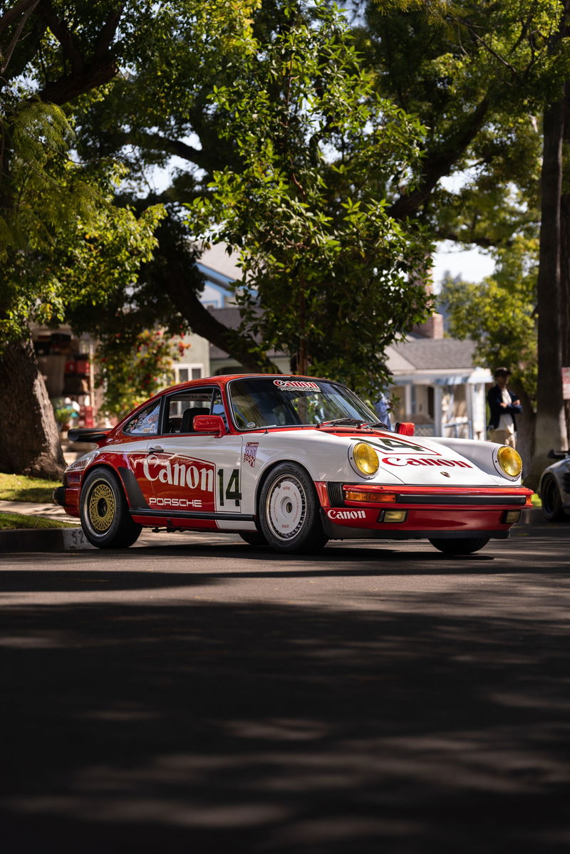 Canon-liveried Porsche 911 Carrera, featuring gold and white rims, red trim, and yellow headlights.