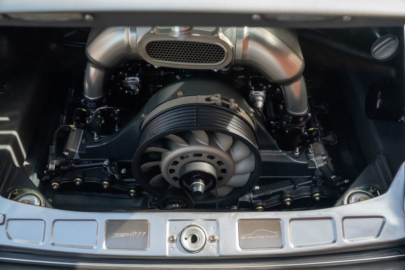 Close-up of a silver Porsche 911 engine with polished intake pipes and a visible fan.