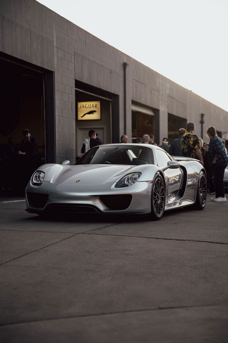 Silver Porsche 918 Spyder with black rims, parked outside Jaguar dealership.