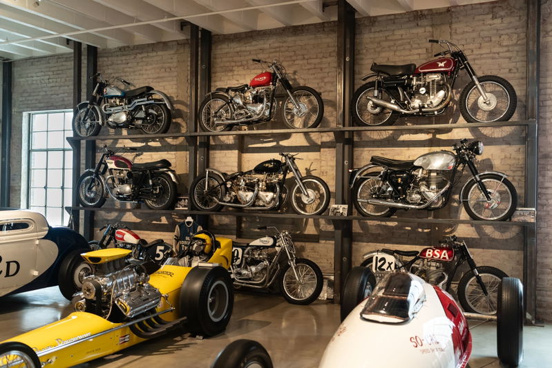 Vintage motorcycles and a yellow dragster on display shelves at the Lit Show Los Angeles 2024.