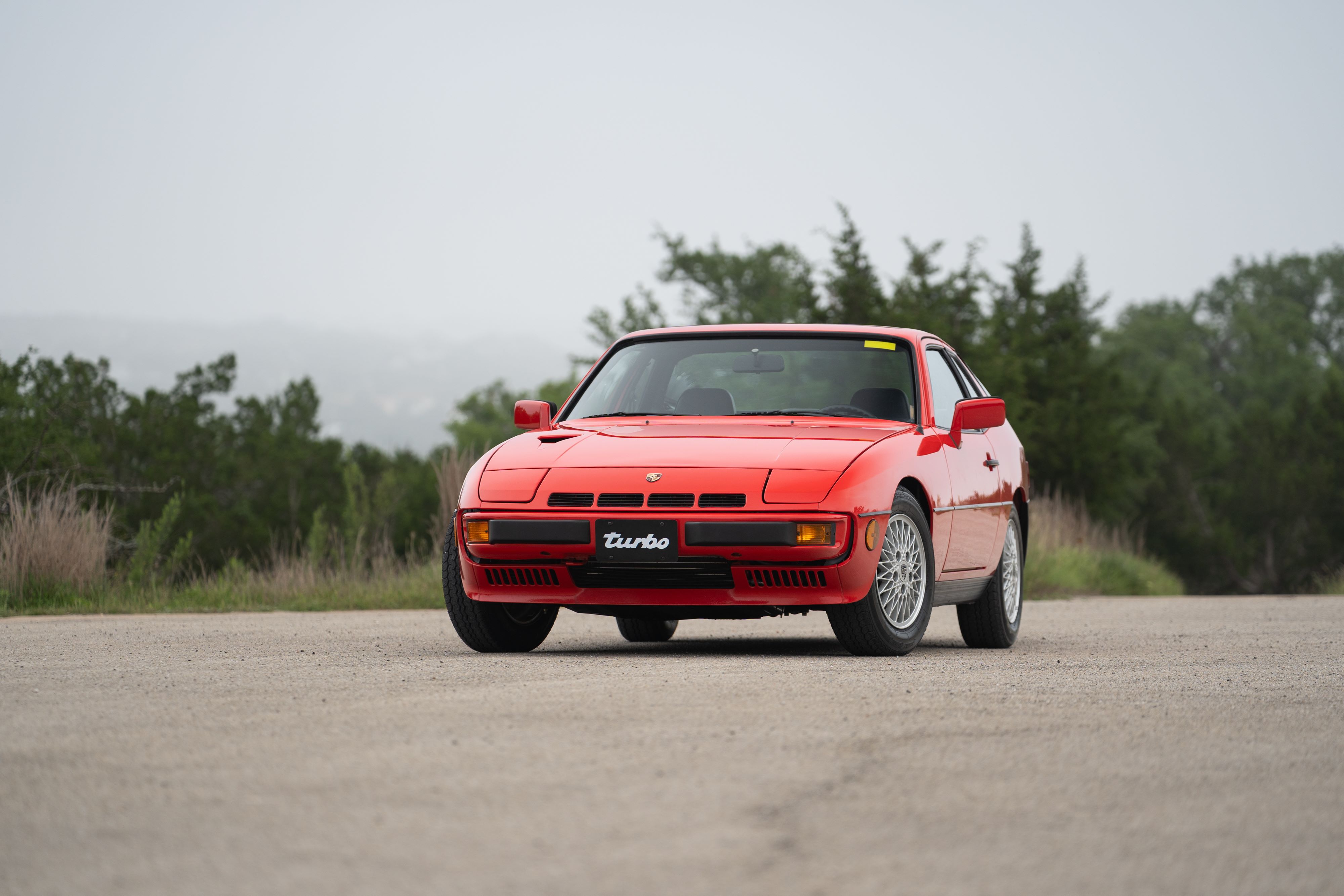 A red 1981 Porsche 924 Turbo sits on asphalt, showcasing its classic front fascia and turbine-style rims.