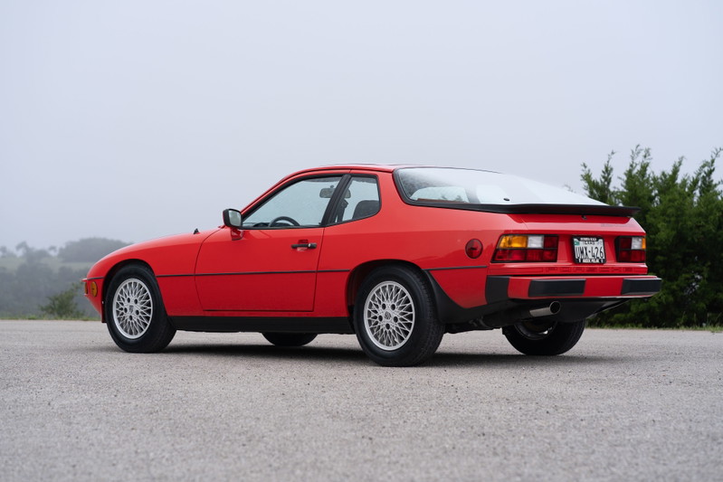 A Guards Red 1981 Porsche 924 Turbo coupe, rear quarter view, with silver alloy rims and black trim.