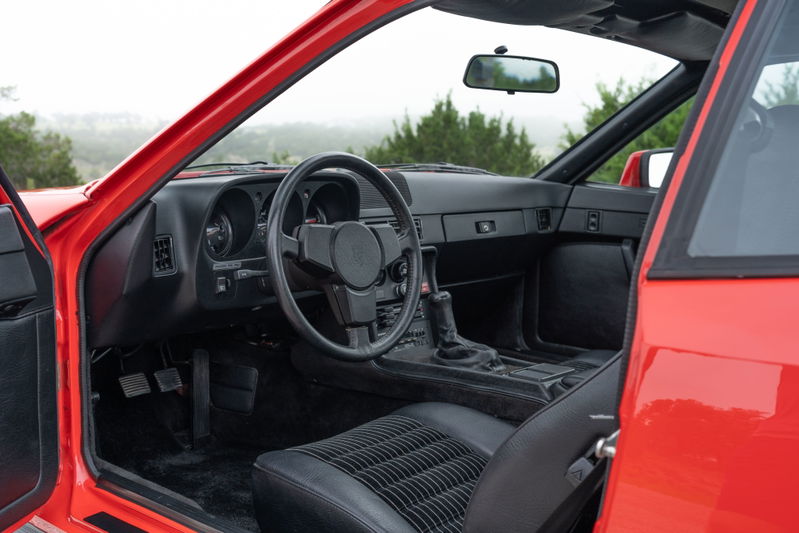 Interior of a Guards Red 1981 Porsche 924 Turbo, featuring black leather seats and a manual transmission shifter.