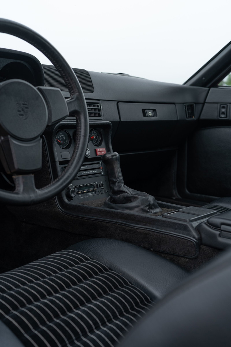 Interior shot of a 1981 Porsche 924 Turbo, black leather interior with striped seats and manual shifter.