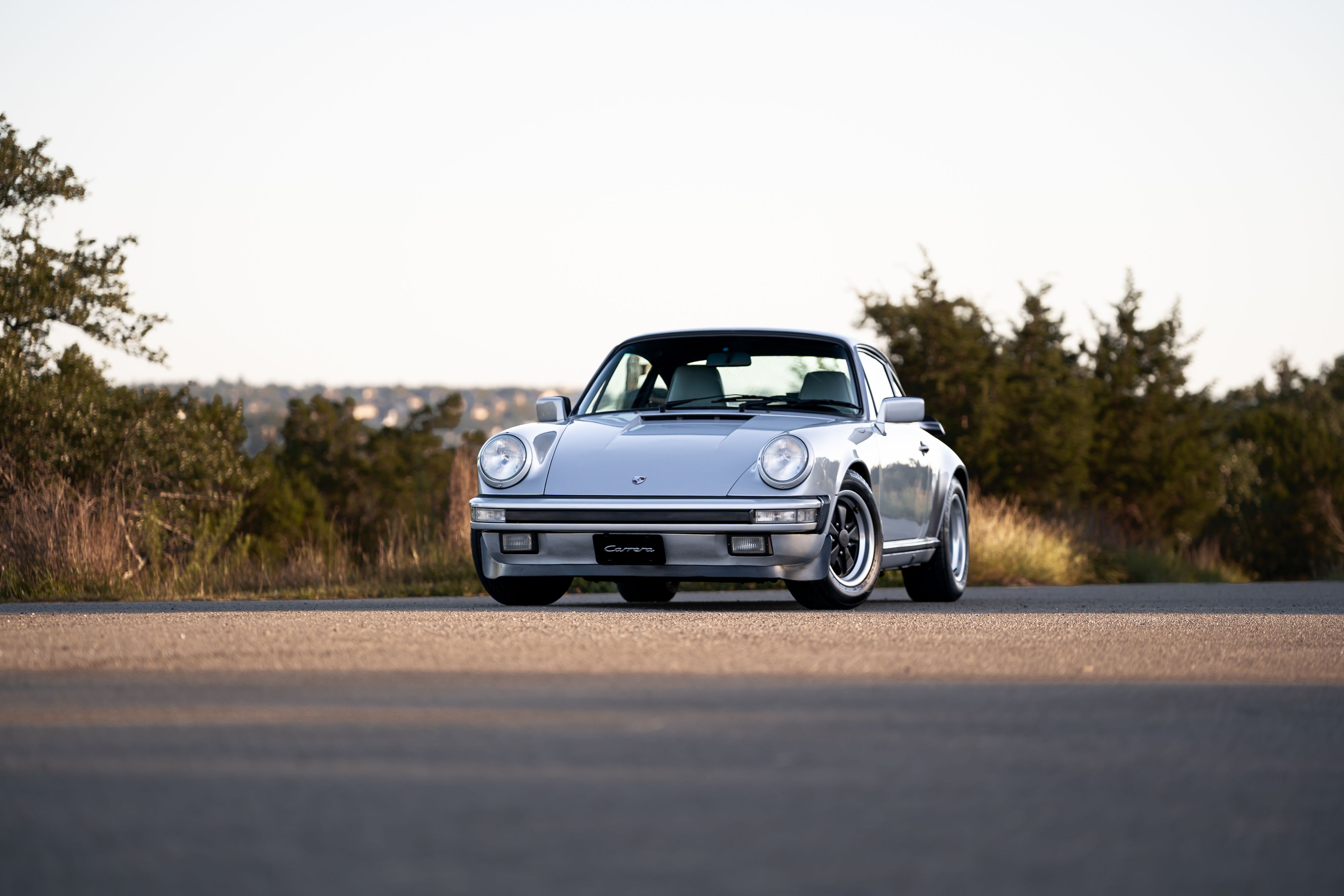 Silver metallic 1987 Porsche 911 Carrera G50 coupe with Fuchs rims parked on asphalt.