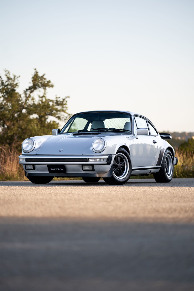 1987 silver metallic Porsche 911 Carrera, front view, with black Fuchs rims and black trim.