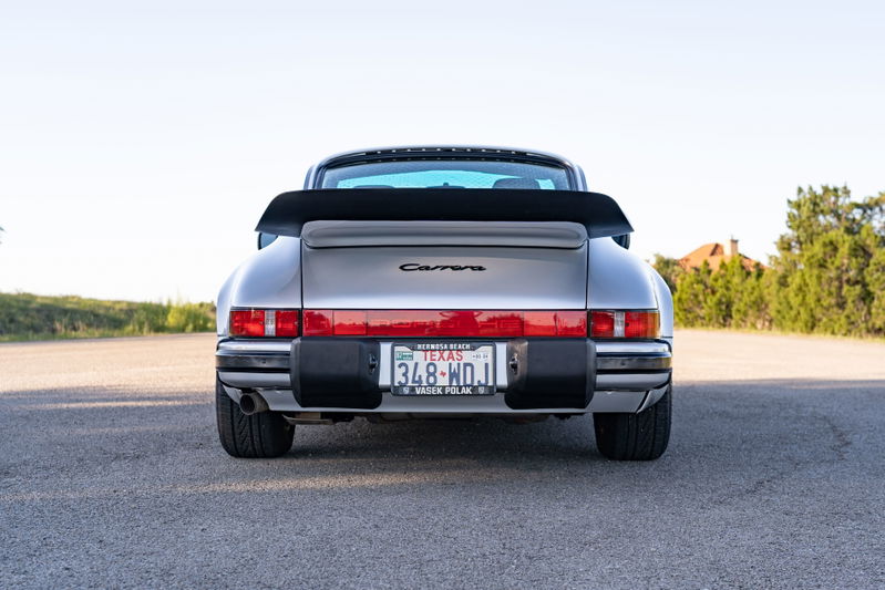 Rear view of a silver 1987 Porsche 911 Carrera with a black whale tail spoiler and Fuchs wheels.