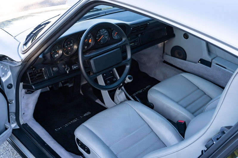 Interior of a silver 1987 Porsche 911 Carrera G50 with gray leather seats and black Porsche floor mats.