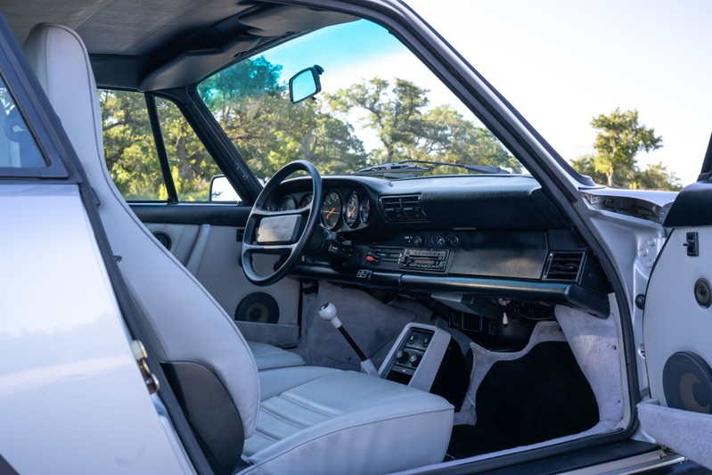 Interior view of a 1987 Porsche 911 Carrera in silver metallic, showing light gray seats and dashboard.