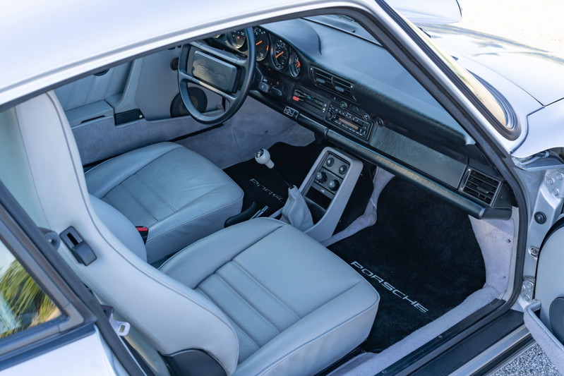 Interior view of a silver 1987 Porsche 911 Carrera G50, featuring light grey leather seats and Porsche floor mats.