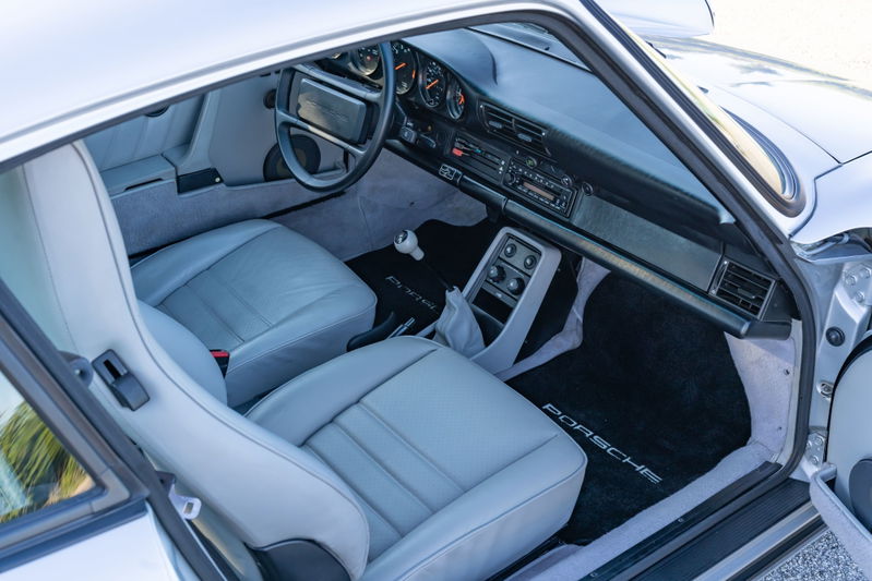 Interior view of a silver 1987 Porsche 911 Carrera G50, featuring light grey leather seats and Porsche floor mats.