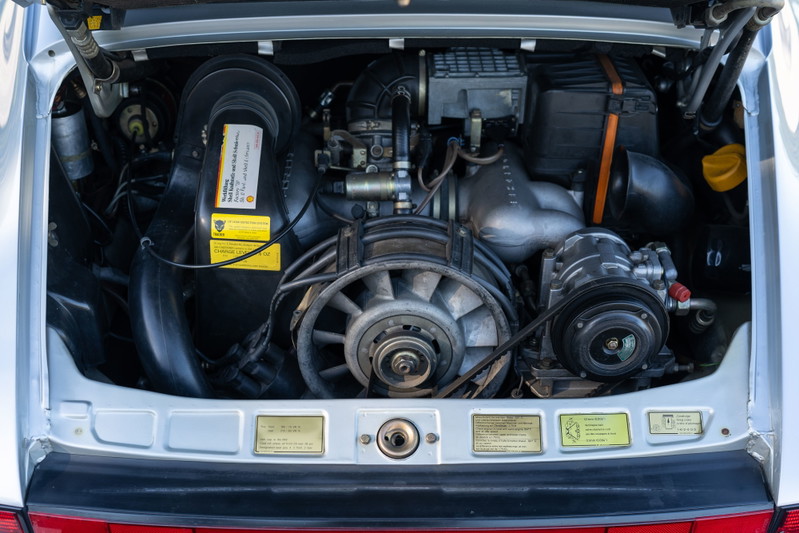 Silver 1987 Porsche 911 Carrera G50 engine bay with air-cooled flat-six, fan, and A/C compressor.