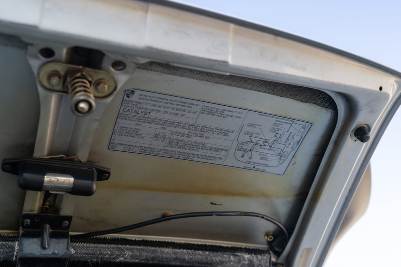 1987 Porsche 911 Carrera hood latch and emissions label, silver metallic exterior trim.