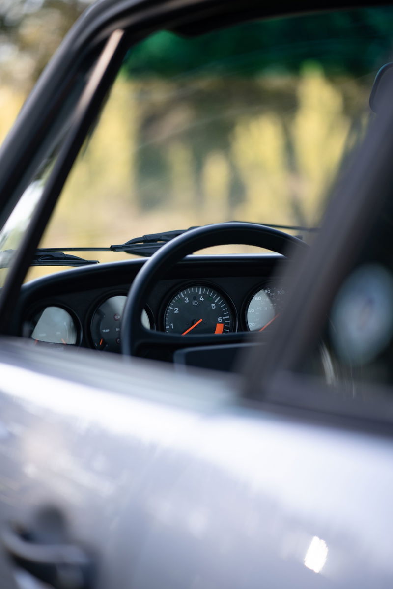 Close-up of a silver 1987 Porsche 911 Carrera G50 dashboard with a black steering wheel and analog gauges.