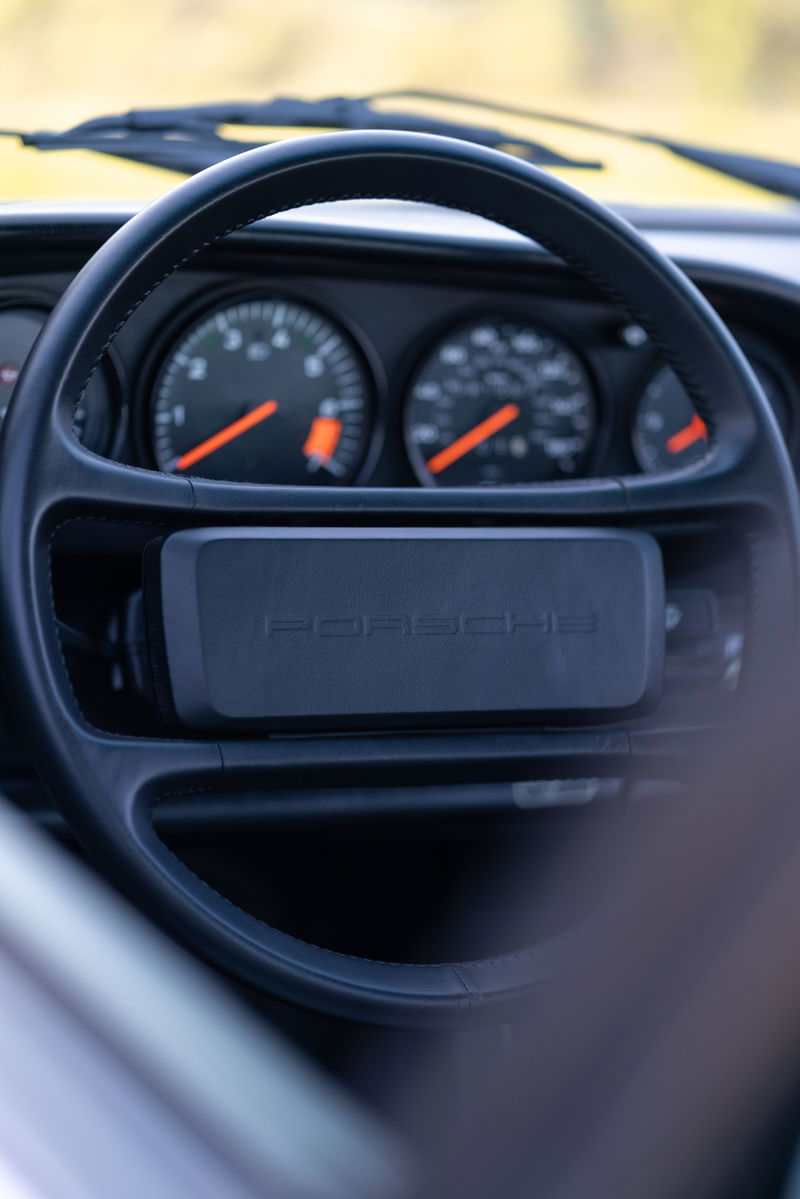 Interior shot of a silver 1987 Porsche 911 Carrera G50 showing the steering wheel and dashboard gauges.