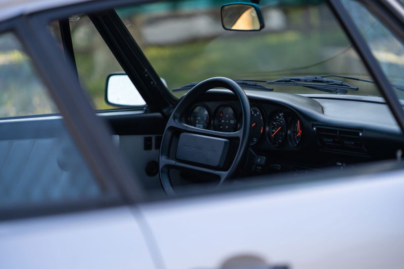 Interior of a 1987 silver Porsche 911 Carrera, showing the dashboard and steering wheel.