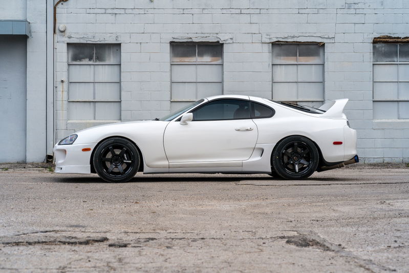 White 1994 Toyota Supra with black rims and a rear wing.