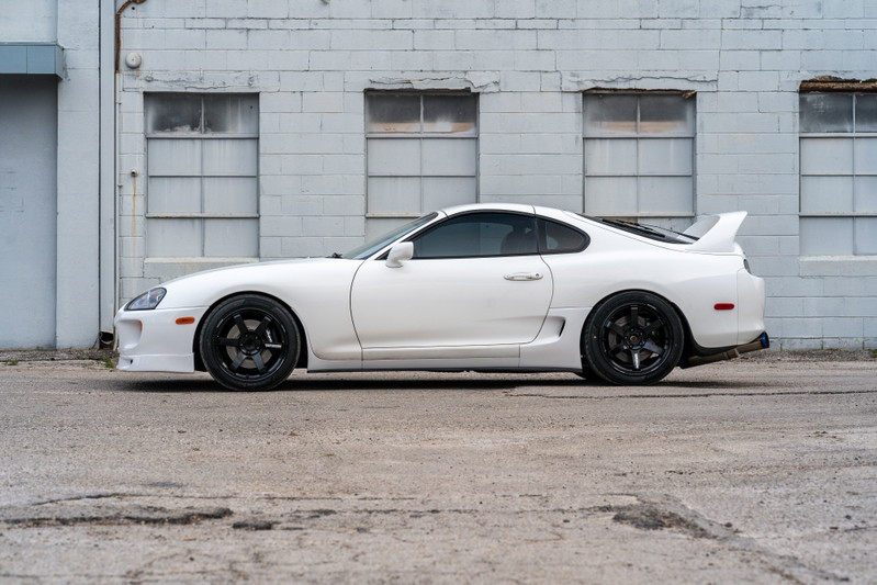 White 1994 Toyota Supra with black rims and a rear wing.
