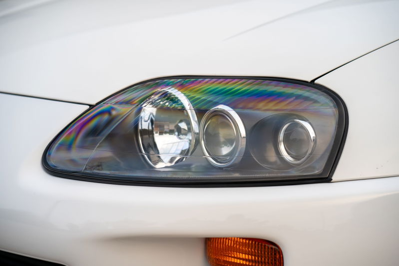 Closeup of a white 1994 Toyota Supra headlight with rainbow prism effect on the lens.