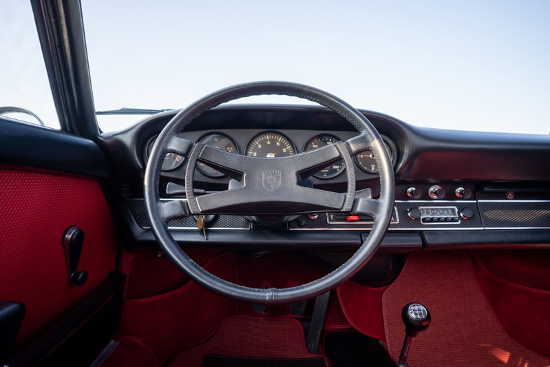 Interior of a blue 1969 Porsche 911S with red upholstery, black steering wheel, and original radio.