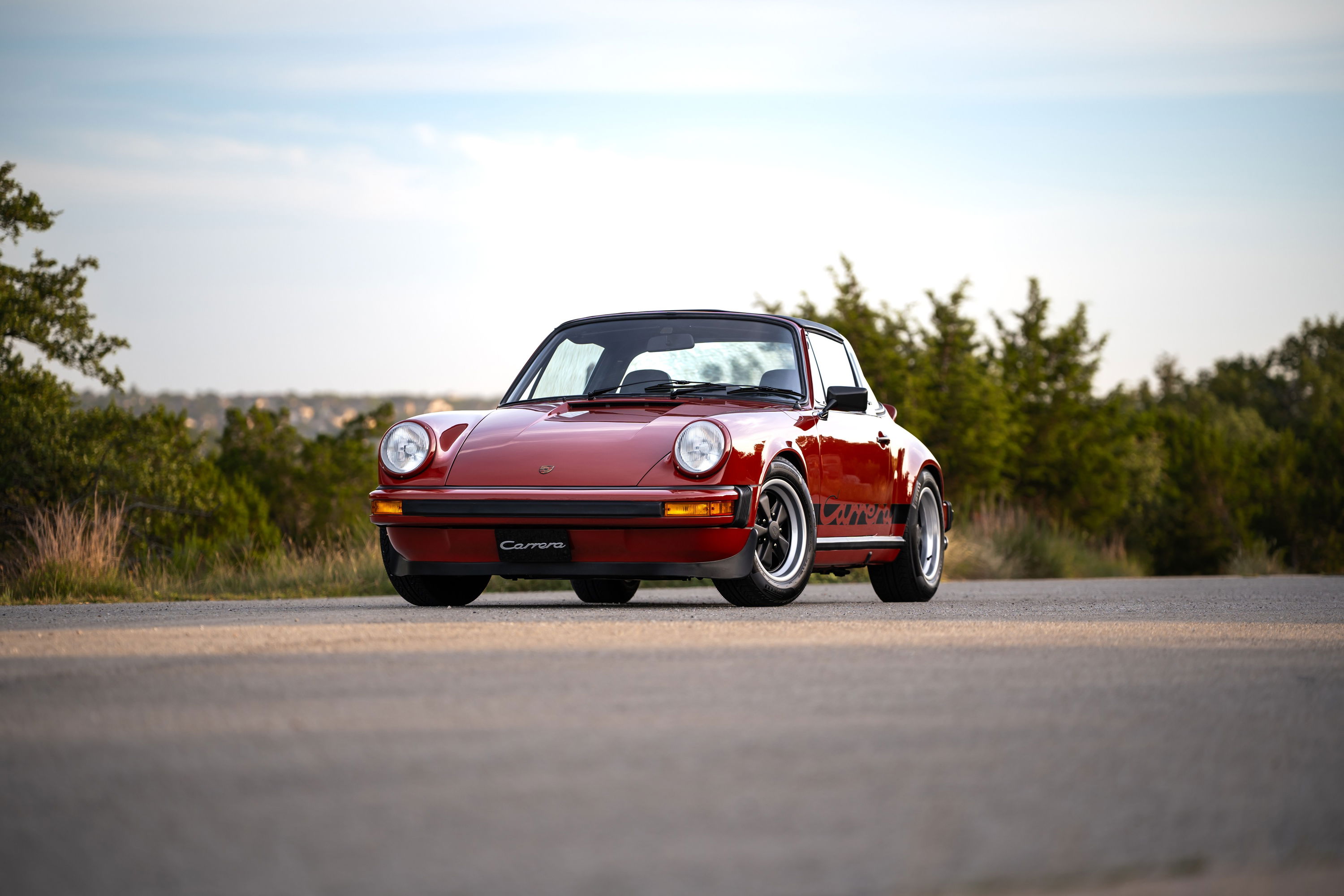 Red 1974 Porsche 911 Carrera Targa with chrome trim and black Fuchs rims.