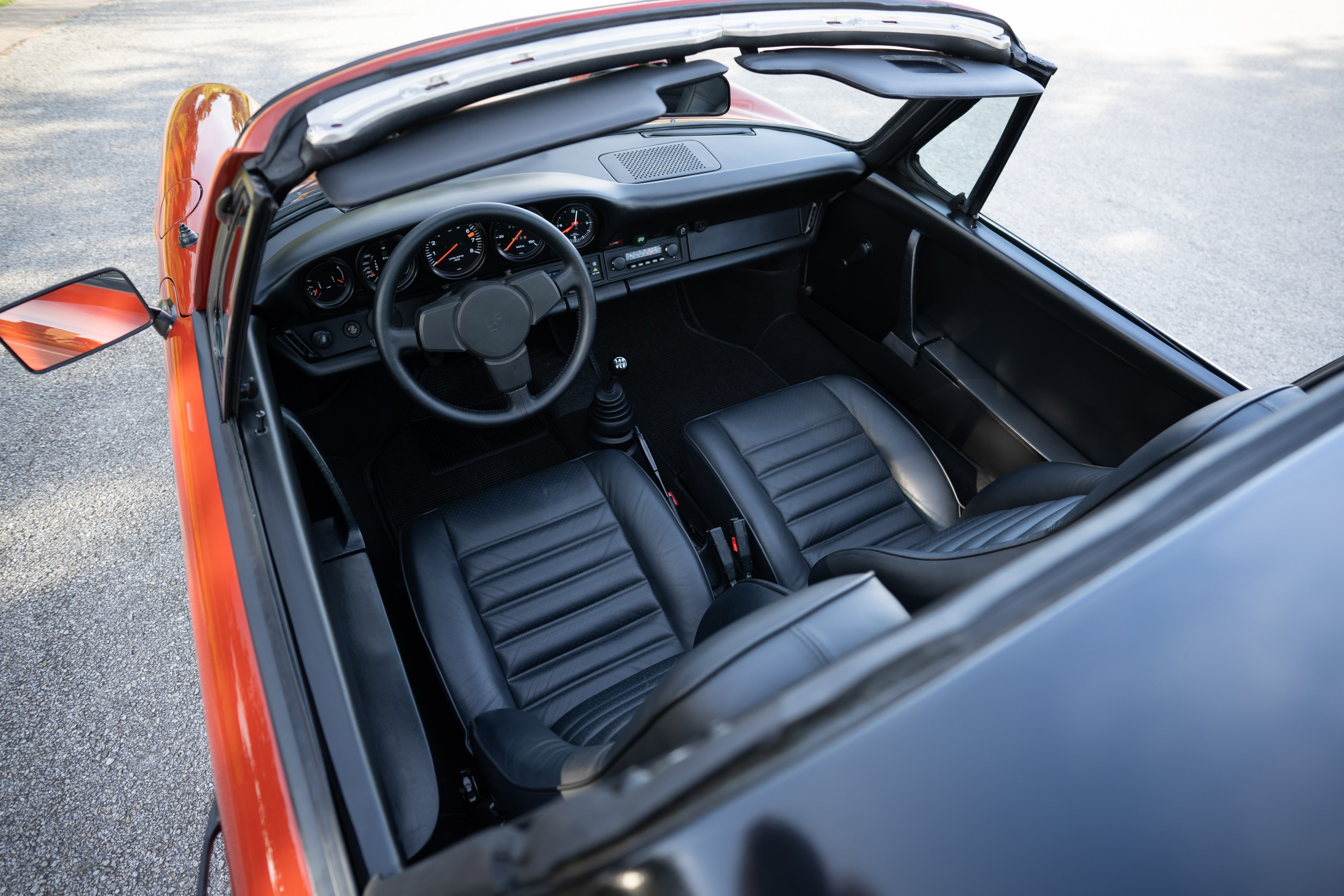Interior view of a red 1974 Porsche 911 Carrera Targa with black leather seats and dashboard.