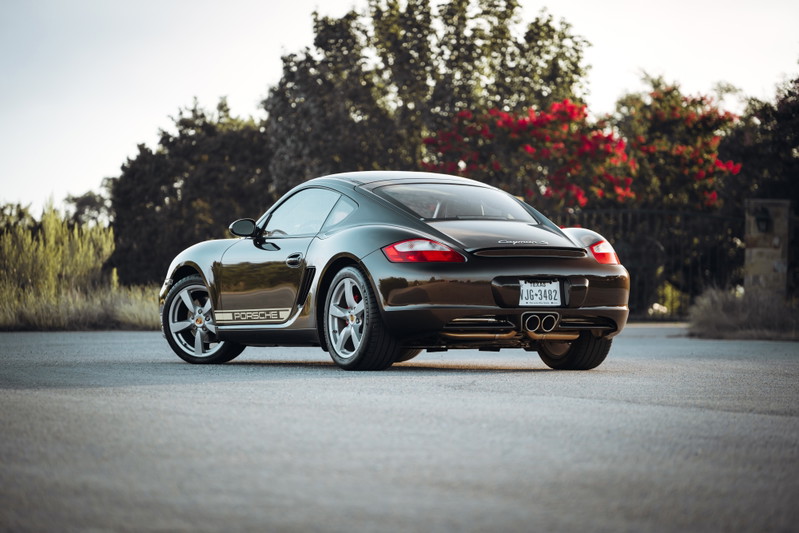 Rear view of a Macadamia Metallic 2008 Porsche Cayman S with silver rims and Porsche livery.