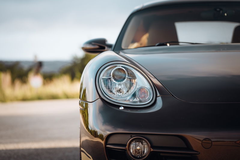Close-up of a Macadamia Metallic 2008 Porsche Cayman S front-end, highlighting the projector headlight.