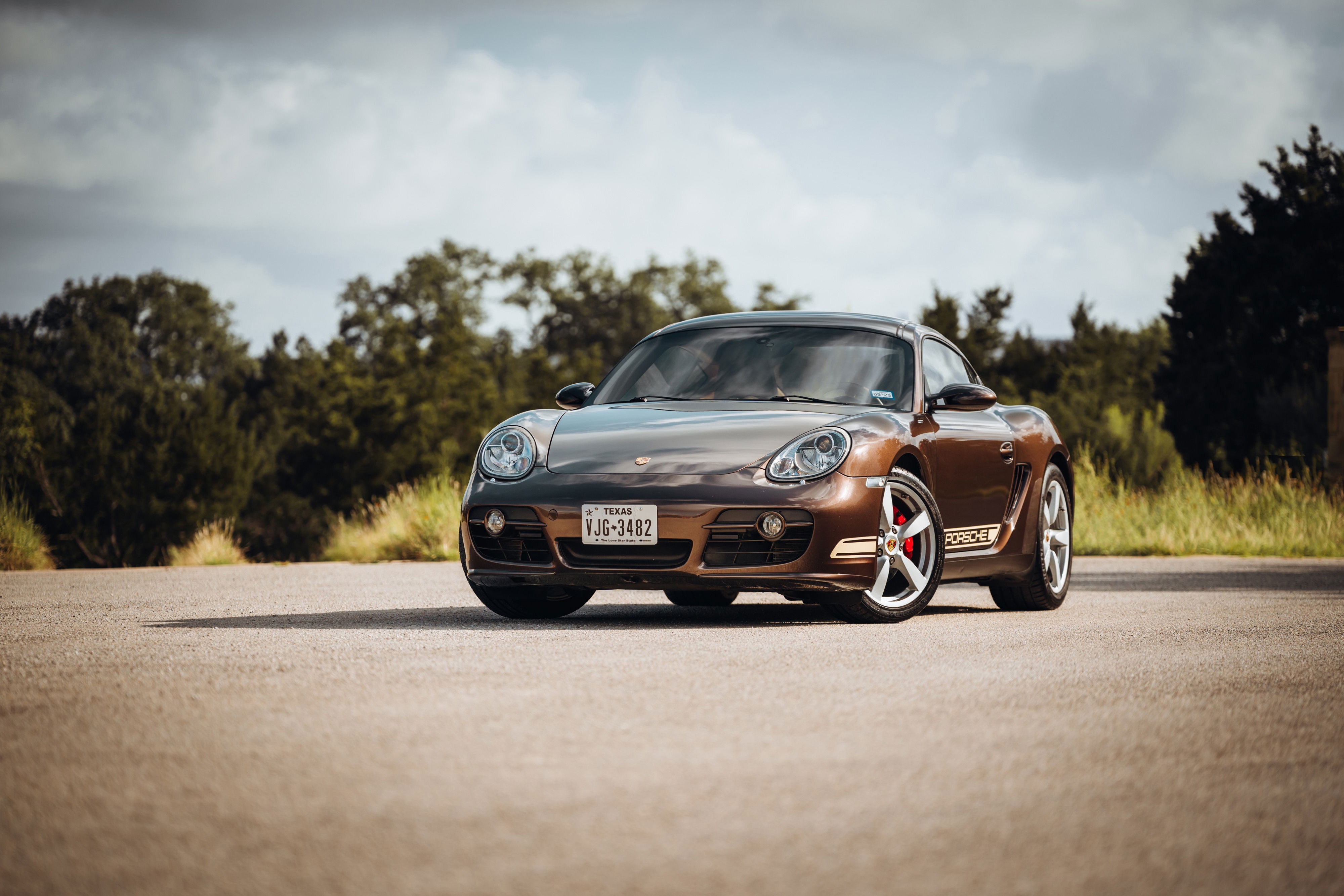 Brown 2008 Porsche Cayman S with silver rims and racing livery.
