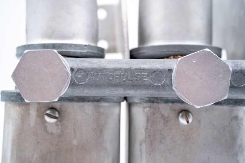 Close-up of an "AUTOPULSE" branded aluminum fitting on a classic Porsche 550 Spyder part.