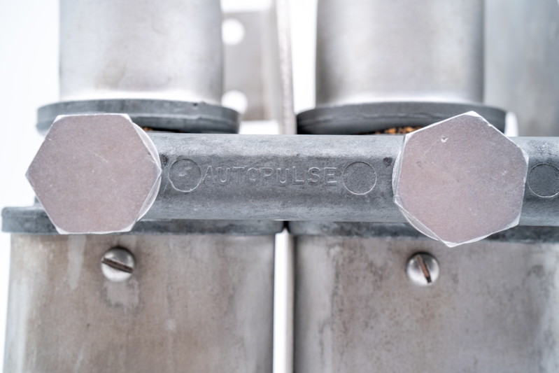 Close-up of an "AUTOPULSE" branded aluminum fitting on a classic Porsche 550 Spyder part.