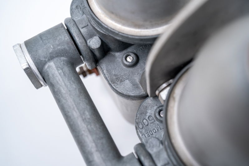 Close-up of a silver 1955 550 Spyder carburetor manifold with "MODEL 500" cast into the aluminum trim.