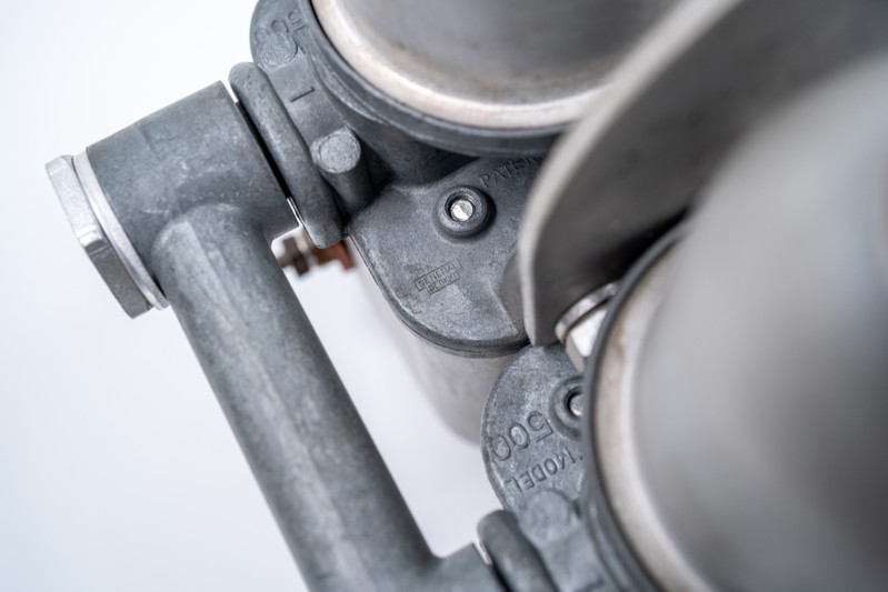 Close-up of a silver 1955 550 Spyder carburetor manifold with "MODEL 500" cast into the aluminum trim.