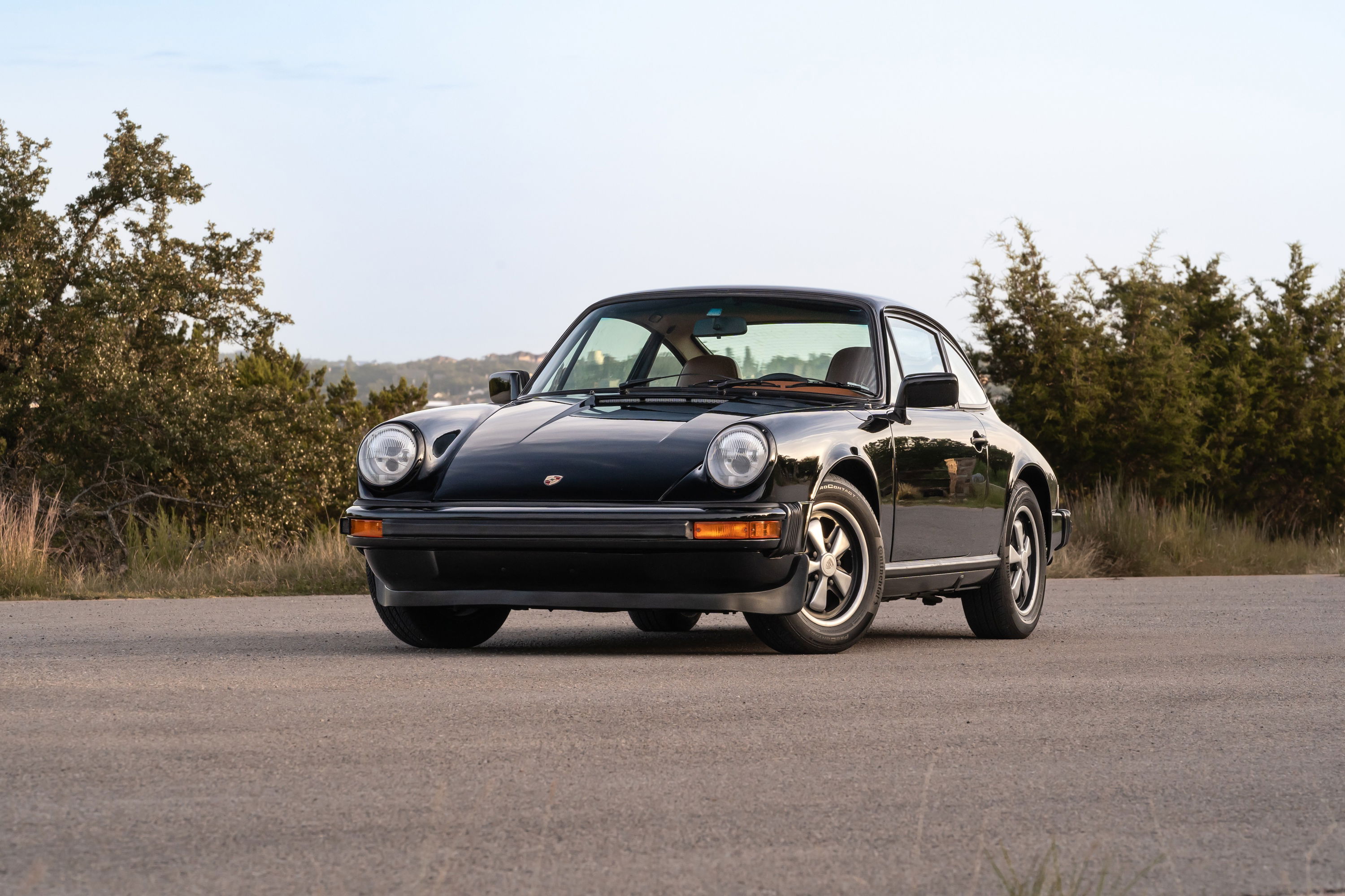 A black 1976 Porsche 911S Sportomatic coupe with alloy rims and chrome trim sits on asphalt.