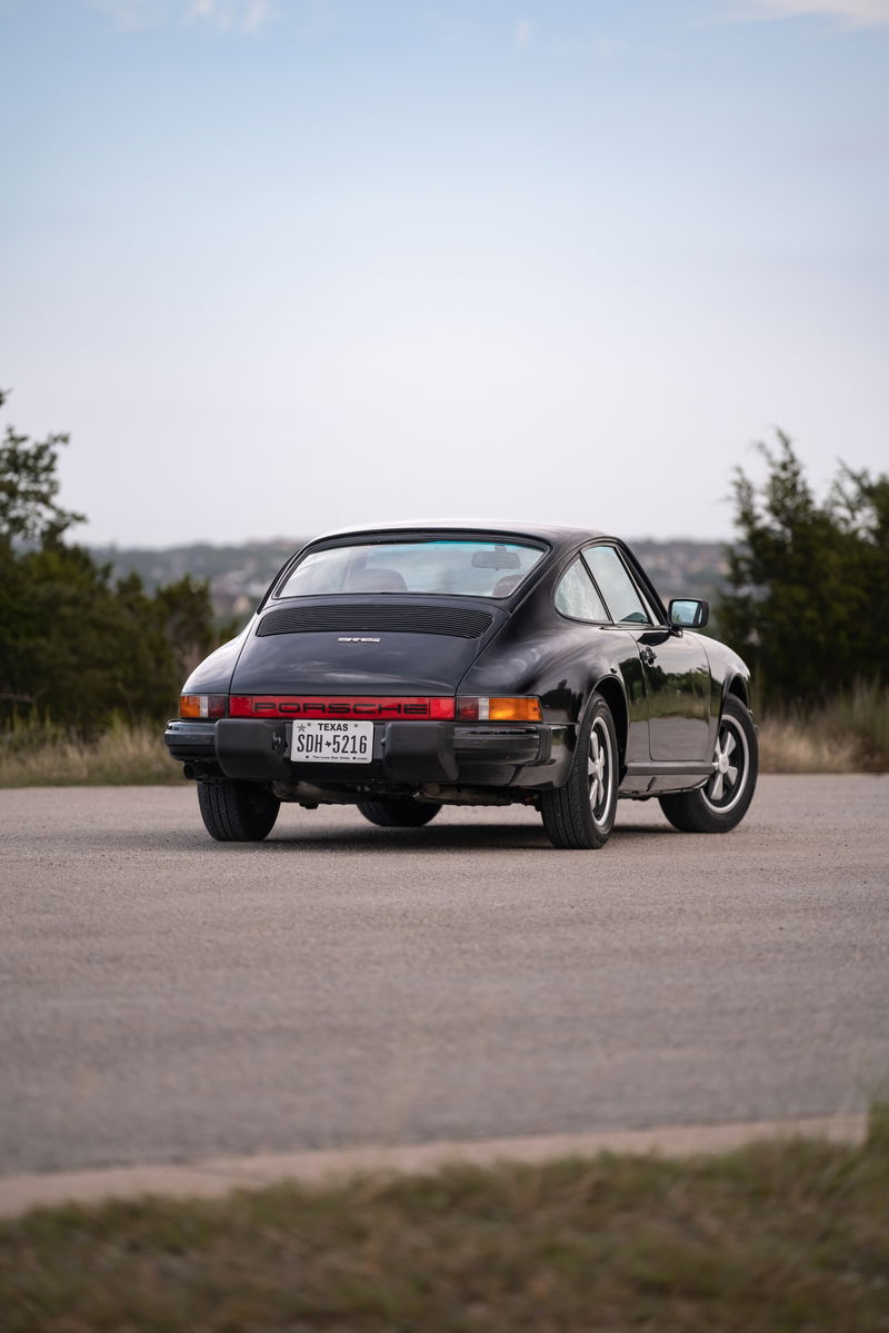 Rear view of a black 1976 Porsche 911S with Fuchs wheels on a paved road.